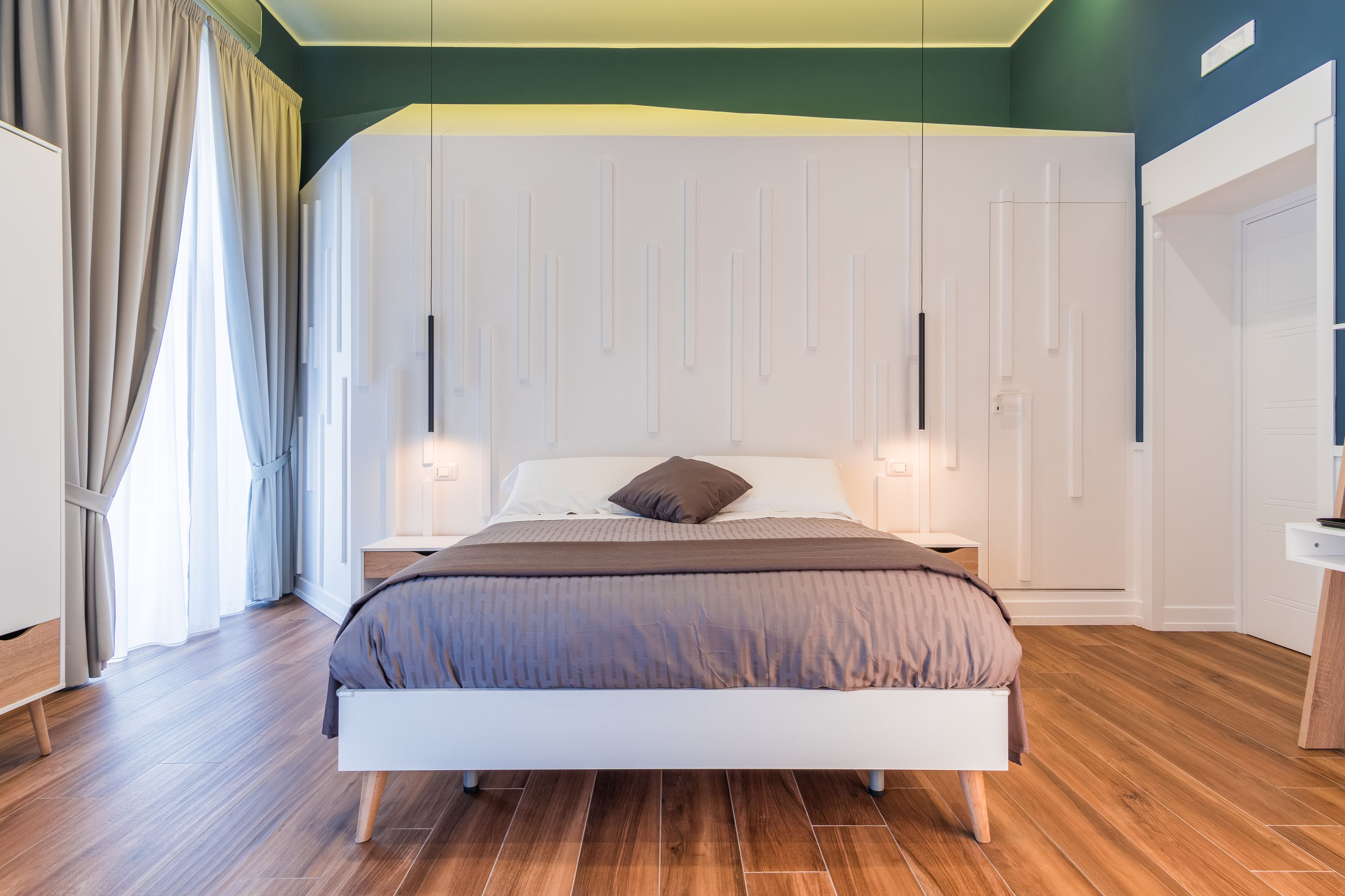 A modern bedroom with a large bed, wooden flooring, and a white wardrobe.