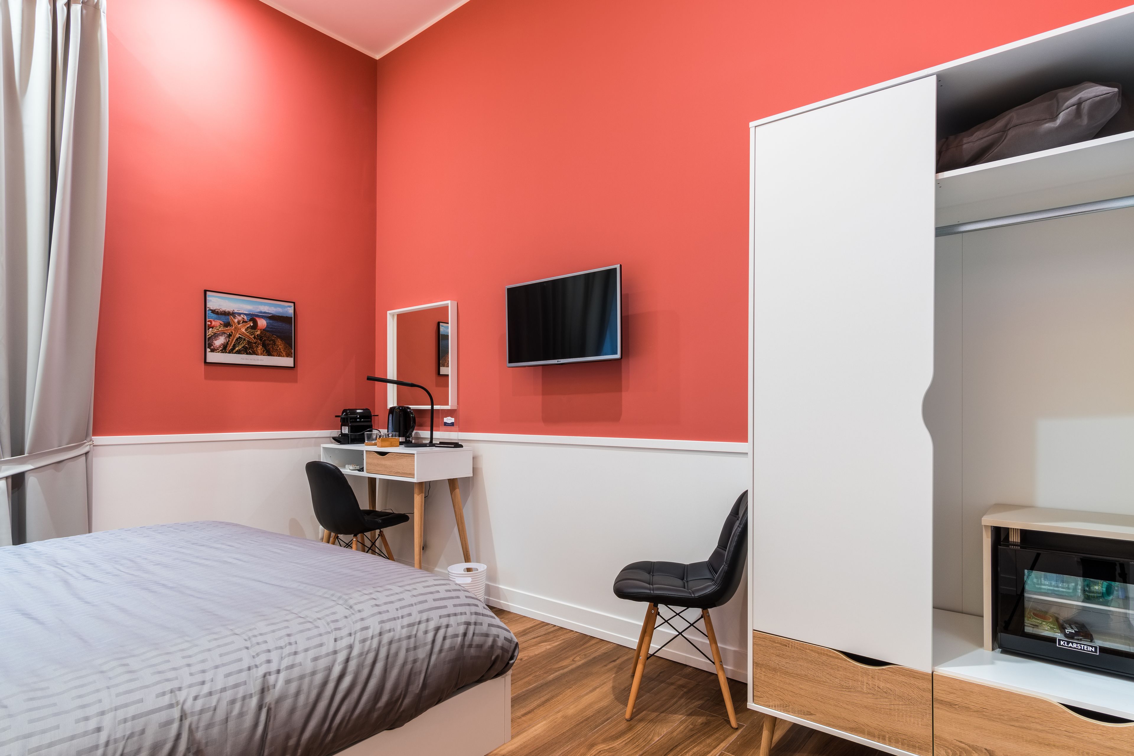 Une pièce de taille modeste comprenant un lit, un bureau avec un ordinateur, une chaise, un téléviseur fixé au mur et une armoire.