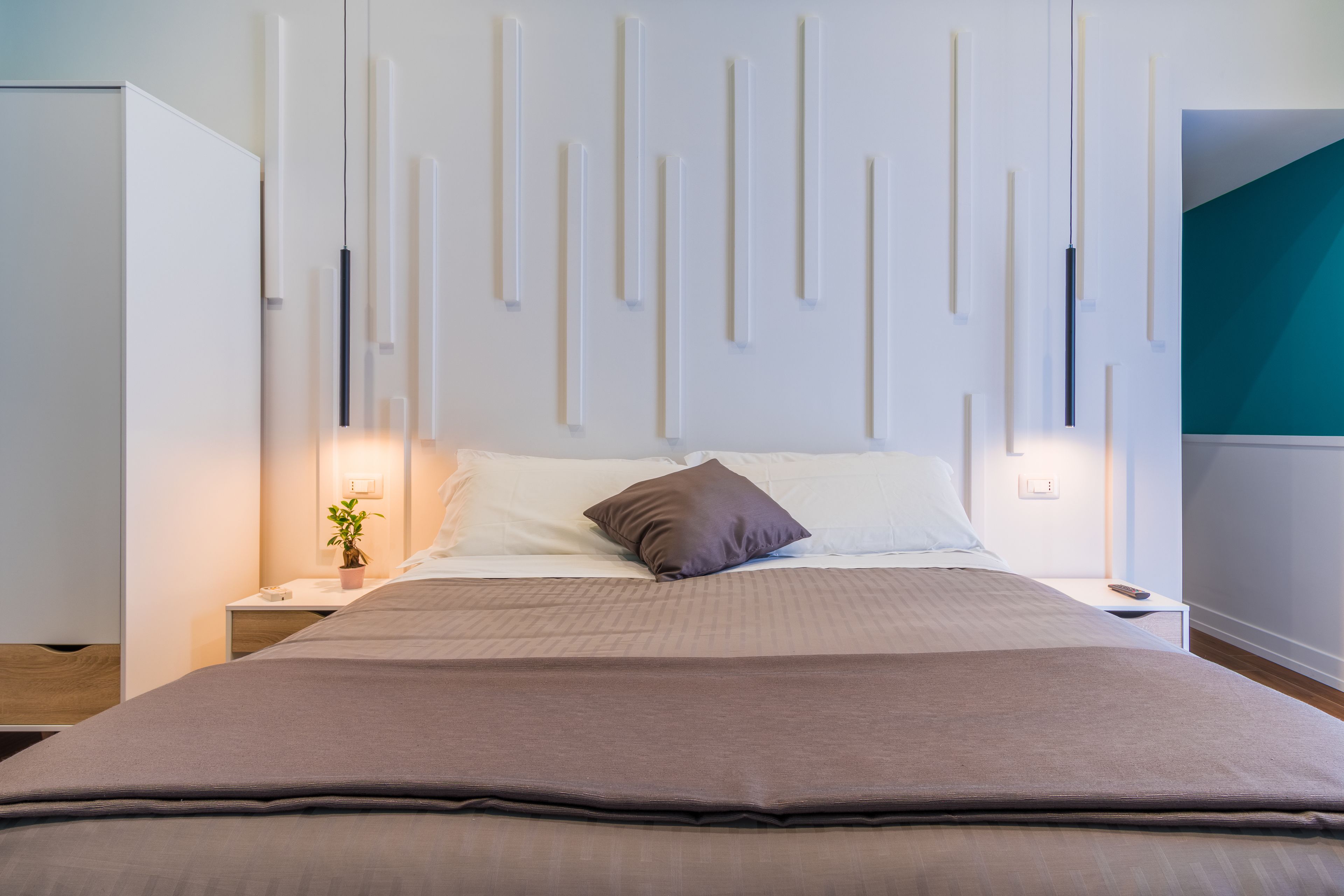 Un dormitorio moderno con una cama grande, mesitas de noche, un aplique de pared y una planta en maceta.