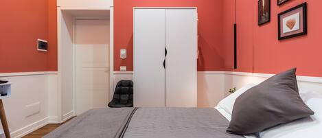 A bedroom with a bed, a chair, a wardrobe, and a door.