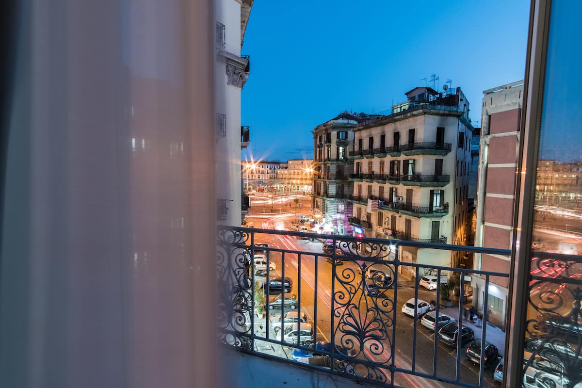 Blick vom Balkon auf eine belebte Straße im Abenddämmerung, mit beleuchteten Gebäuden und Fahrzeugen.