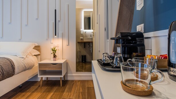 A modern hotel room with a bed, bedside table, and a coffee station with a coffee maker, cups, and a tray. - VistaViva B&B (Naples)