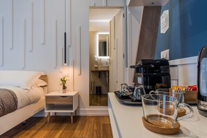 Egy modern szállodai szoba, amelyben található egy ágy, egy éjjeliszekrény, valamint egy kávéfőzővel, csészékkel és egy tálcával felszerelt kávészöglet.