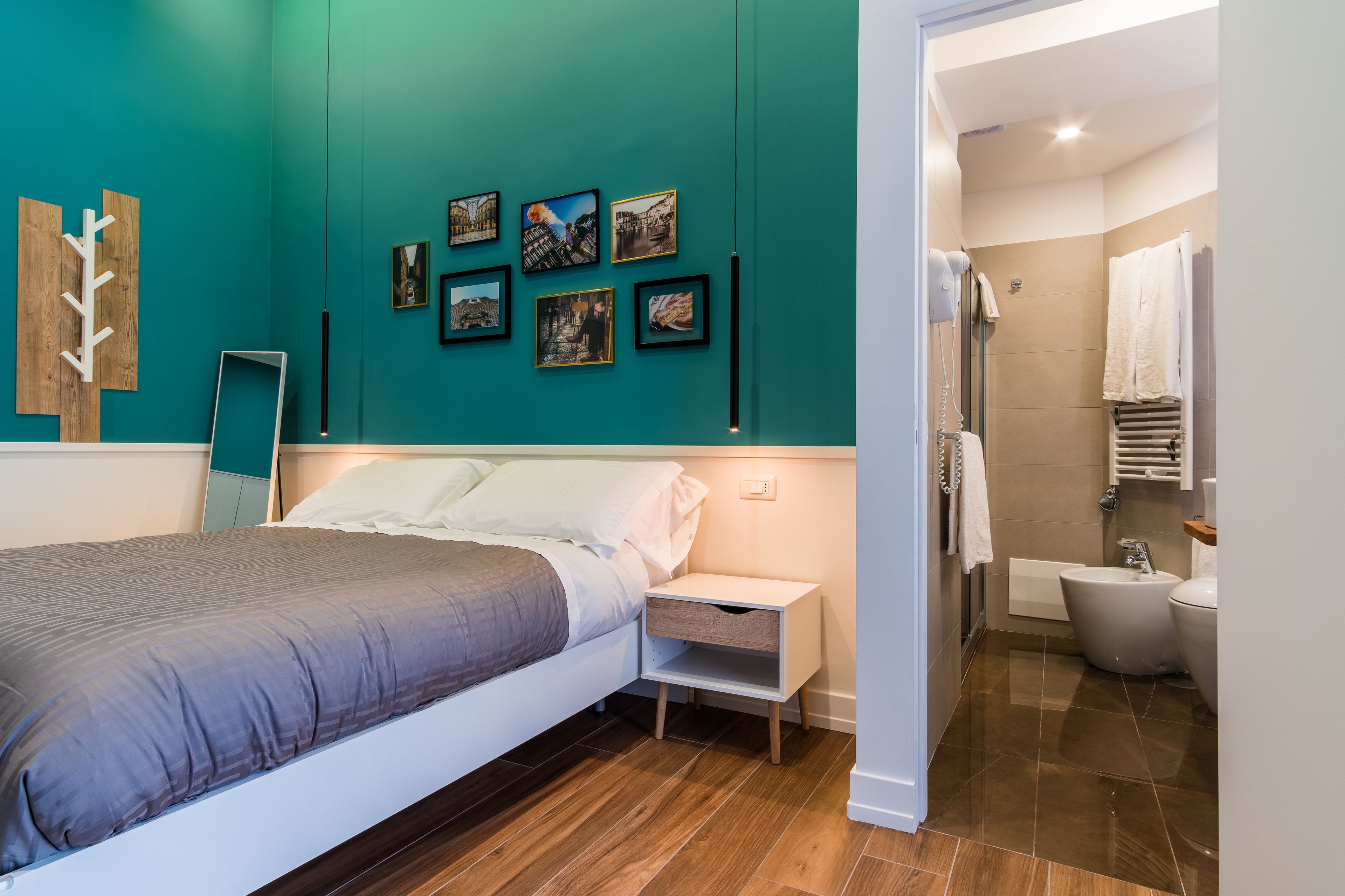 A modern bedroom with a bed, bedside table, and a wall with framed pictures.