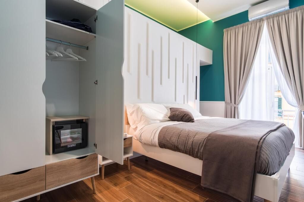 A bedroom with a bed, a wardrobe, a small table, and a window with curtains.