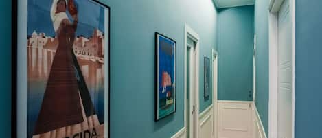 Un pasillo con paredes verde azuladas, obras de arte enmarcadas y puertas blancas.