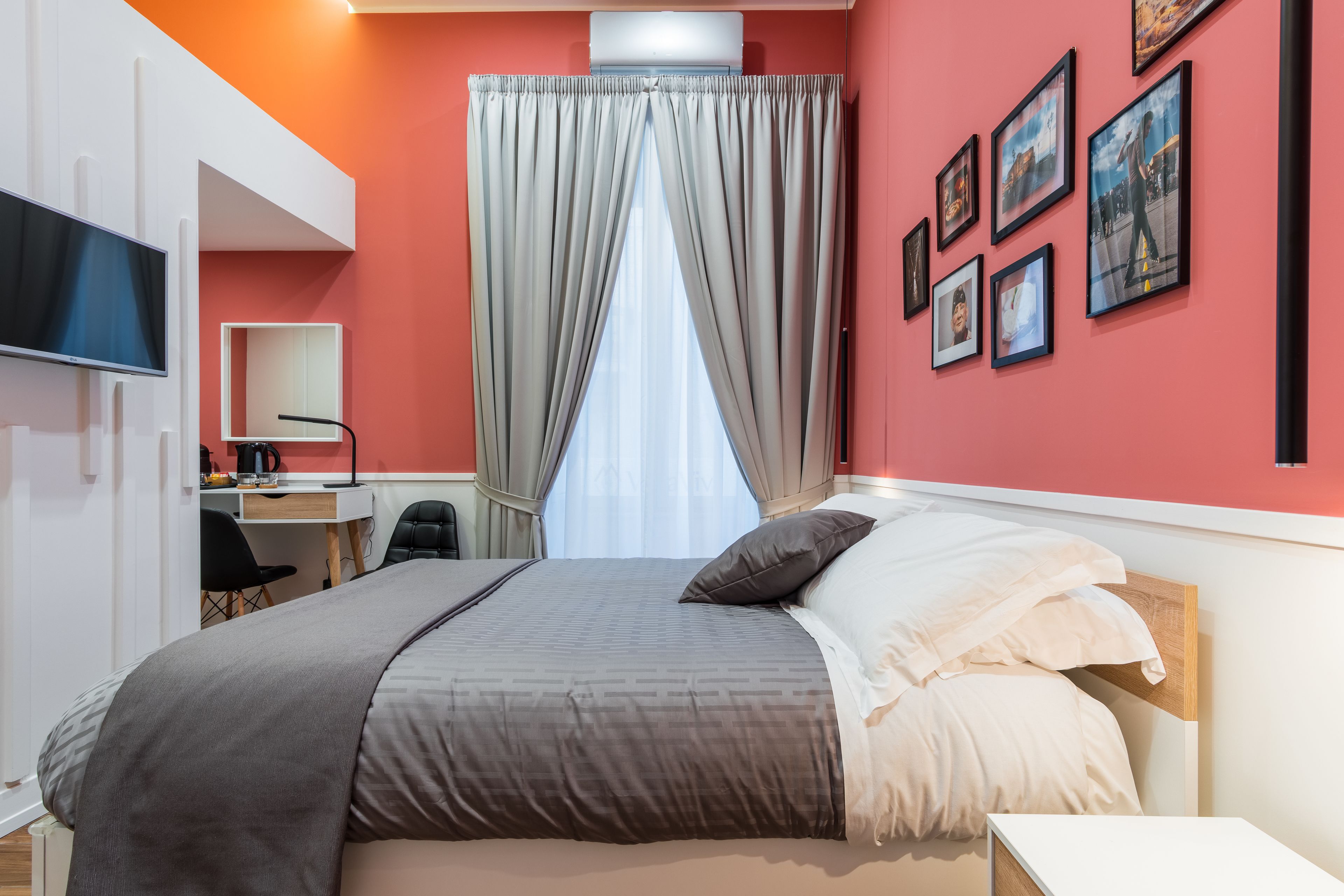 Una habitación de hotel moderna con una cama grande, un escritorio con silla, un televisor y una ventana con cortinas.