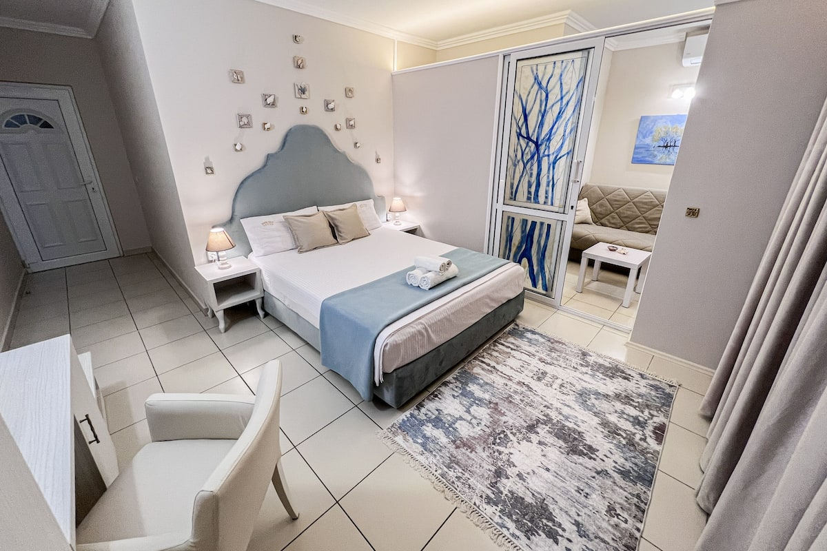 Una habitación de hotel moderna con una cama grande, mesitas de noche, una silla, un sofá y un detalle decorativo en la pared.