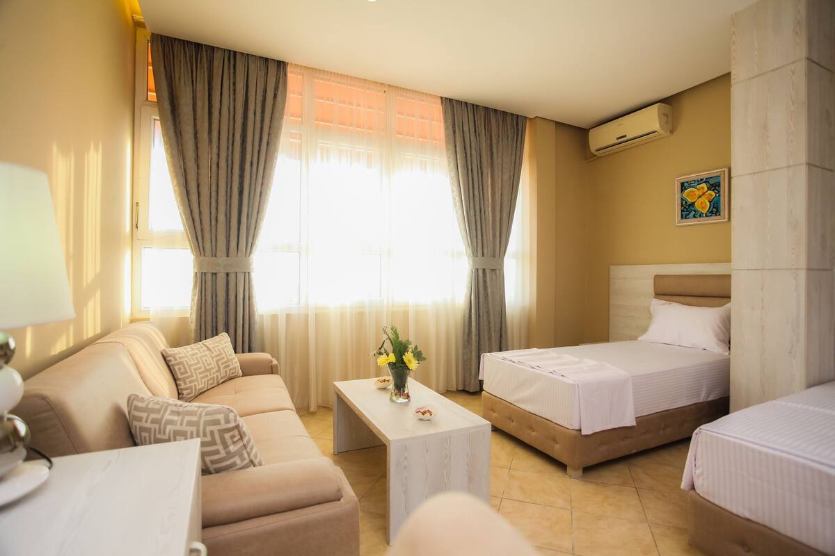 Una habitación de hotel con sofá, dos camas, una mesita de centro y un aire acondicionado.