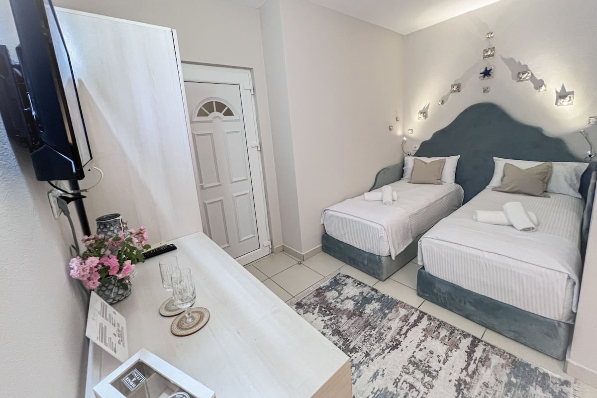 Habitación de hotel con dos camas individuales, un escritorio con una computadora y un florero, y una puerta con un arco decorativo.