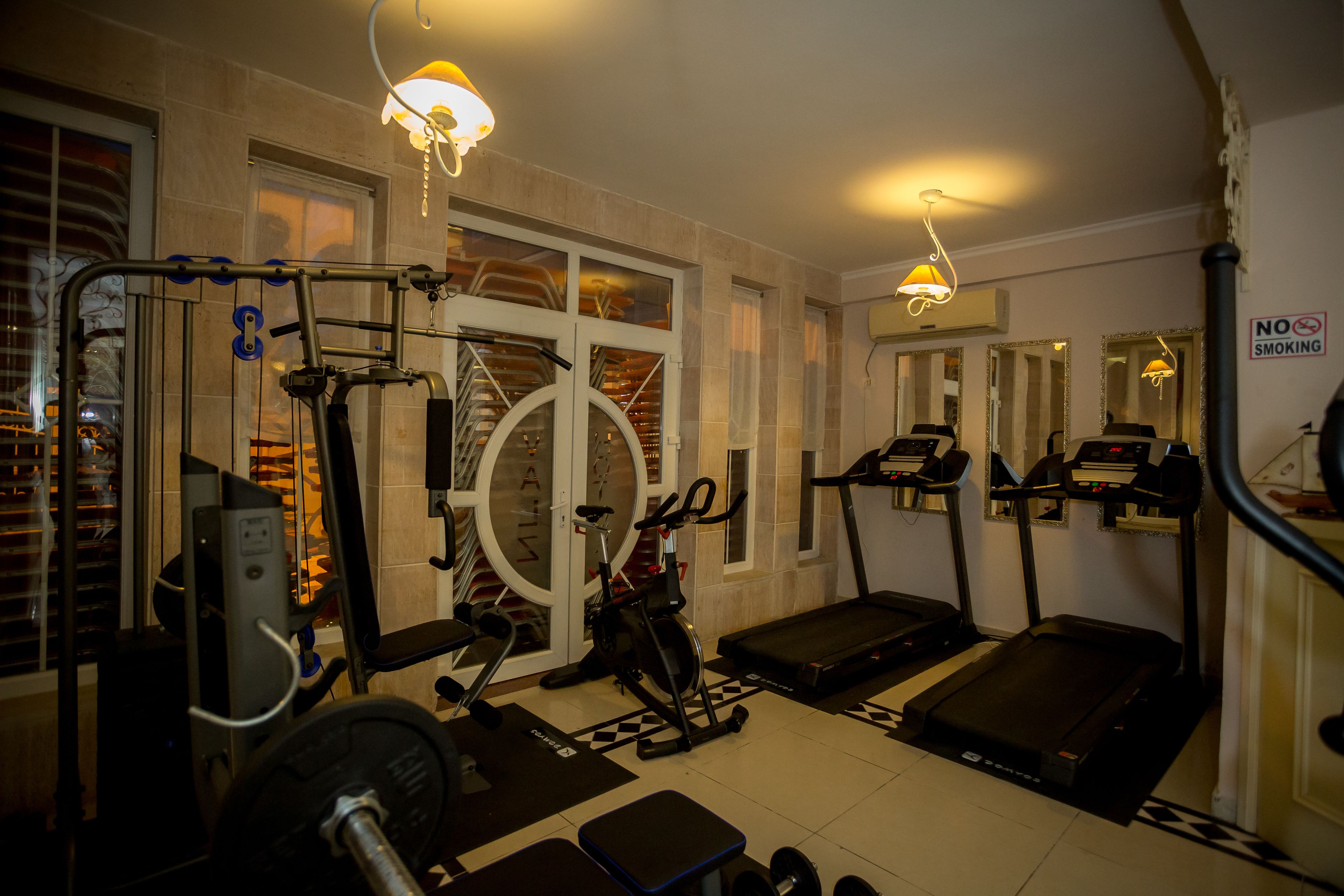 Une salle de sport équipée de matériel d’exercice, d’un tapis de course et d’un panneau indiquant qu’il est interdit de fumer.
