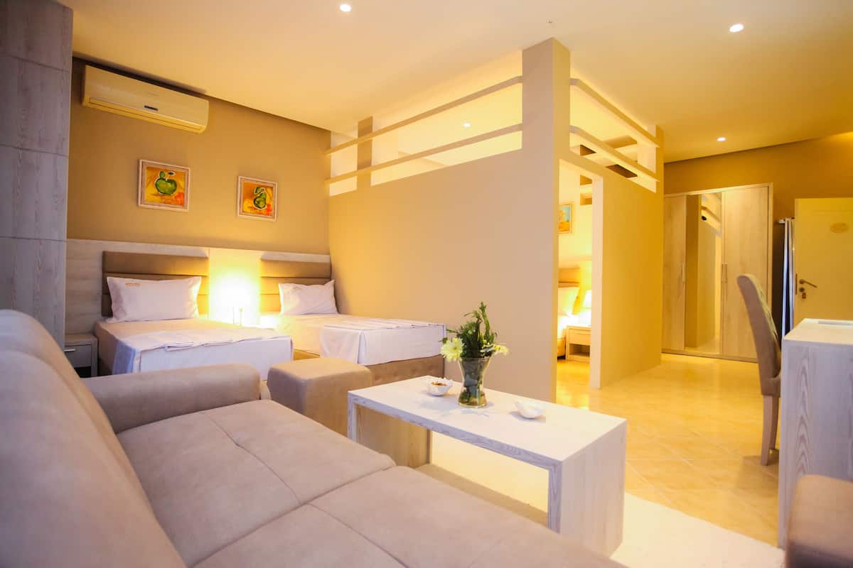 Habitación de hotel con dos camas, un sofá, una mesita y un baño visible a través de una puerta abierta.