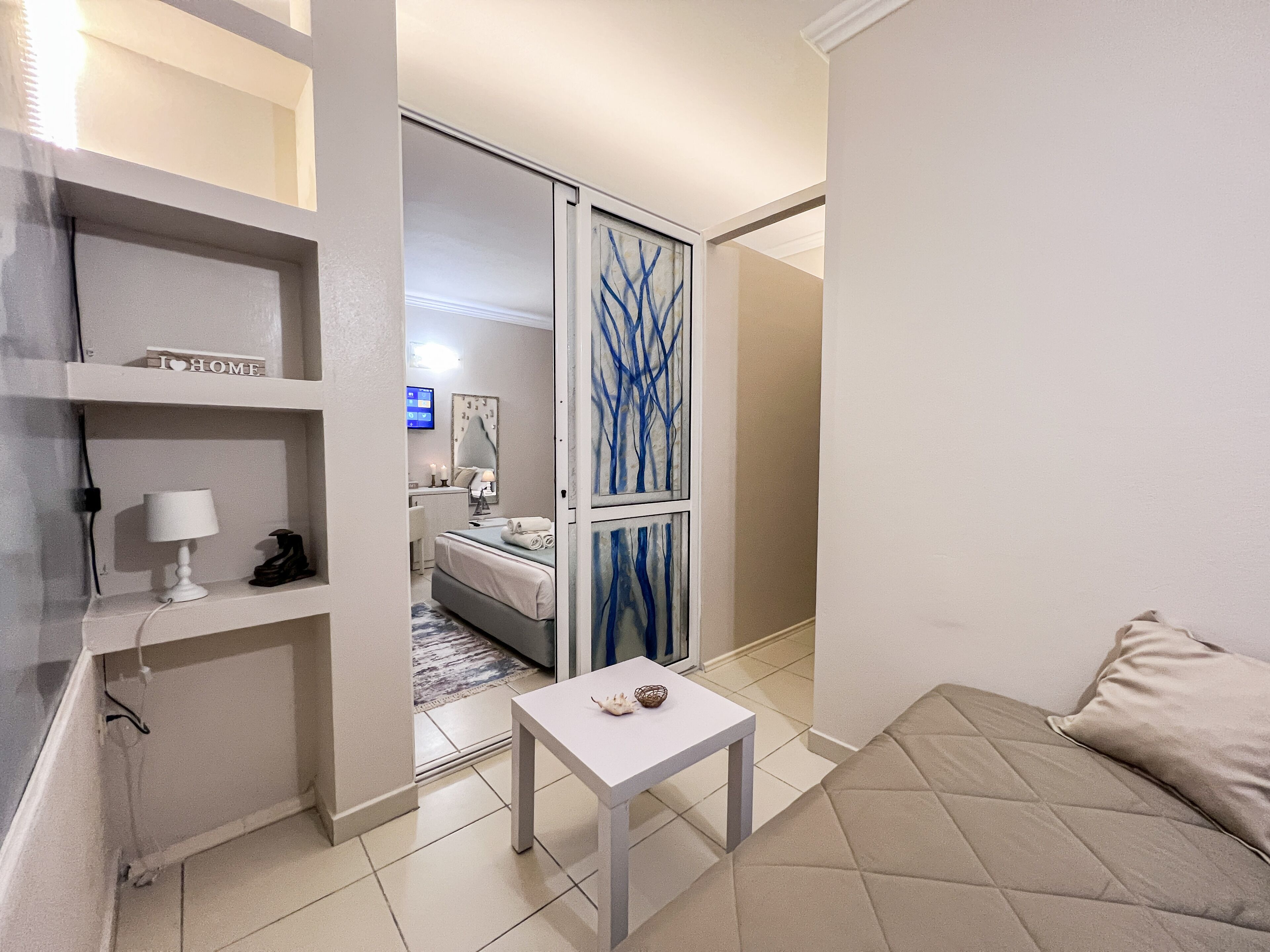 A modern hotel room with a bed, a small table, a desk, and a TV.
