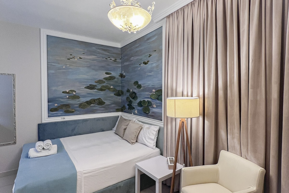 Una habitación de hotel con una cama, un escritorio, una silla, una lámpara y un cuadro de nenúfares.