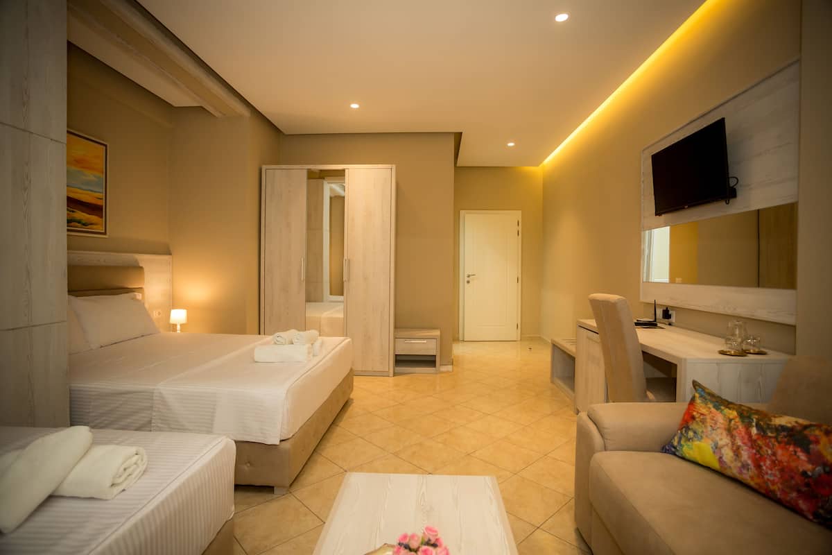 Habitación de hotel con dos camas, un sofá, una mesa de centro, un televisor y un escritorio con una silla.