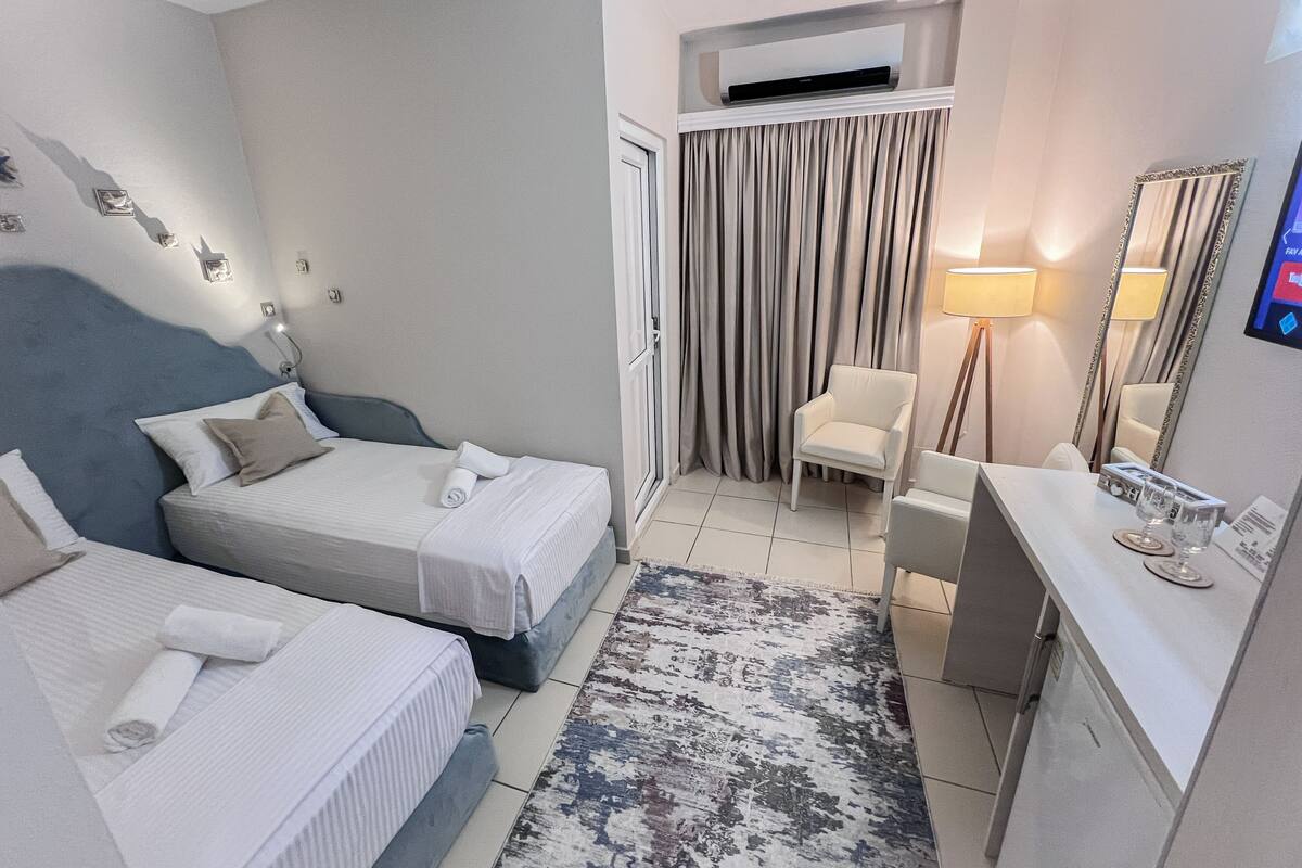 Habitación de hotel con dos camas, un escritorio, una silla, un espejo y un equipo de aire acondicionado.