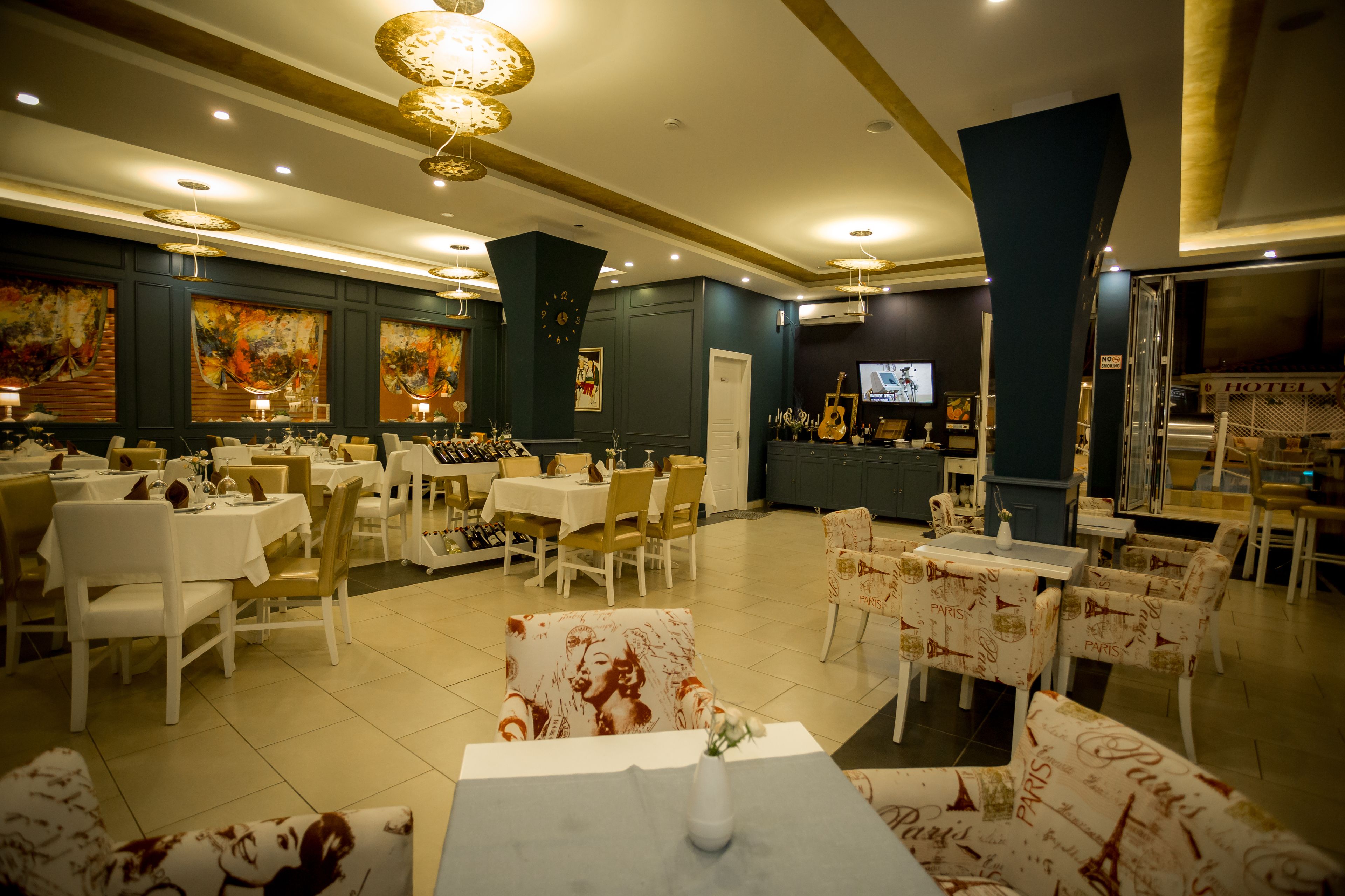 Un comedor de hotel con varias mesas y sillas, un televisor y obras de arte en las paredes.