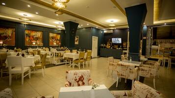 Un comedor de hotel con varias mesas y sillas, un televisor y obras de arte en las paredes.