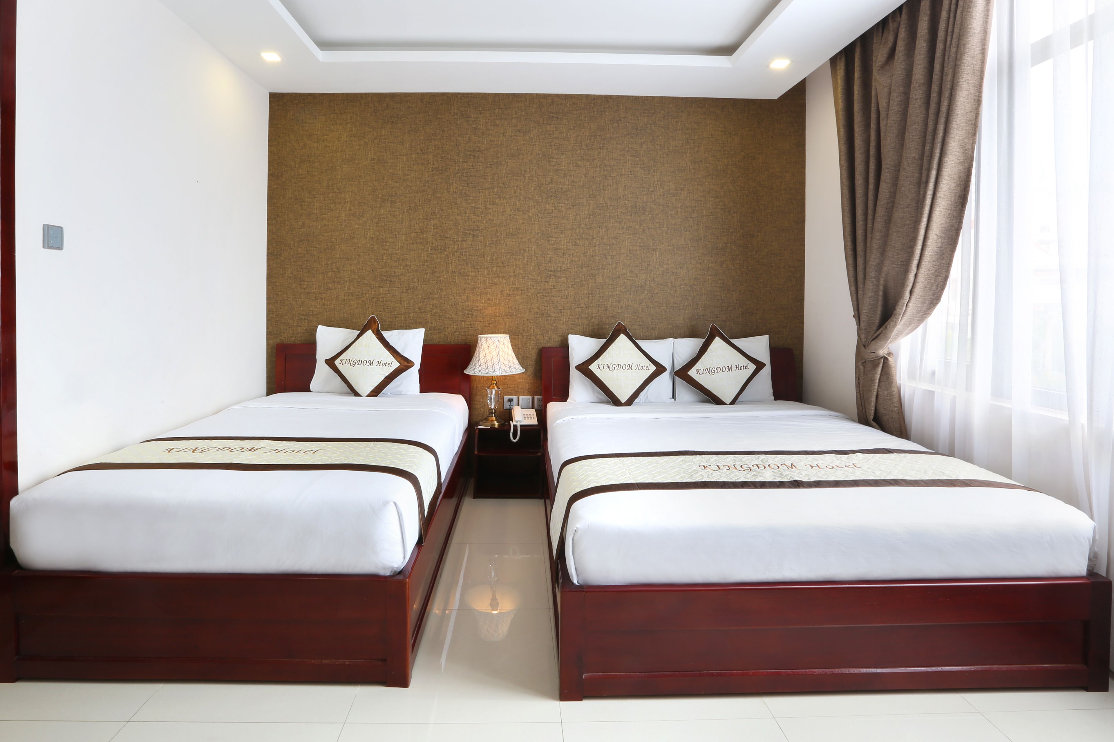 Une chambre d’hôtel avec deux lits, une table de chevet avec une lampe et une grande fenêtre avec des rideaux.