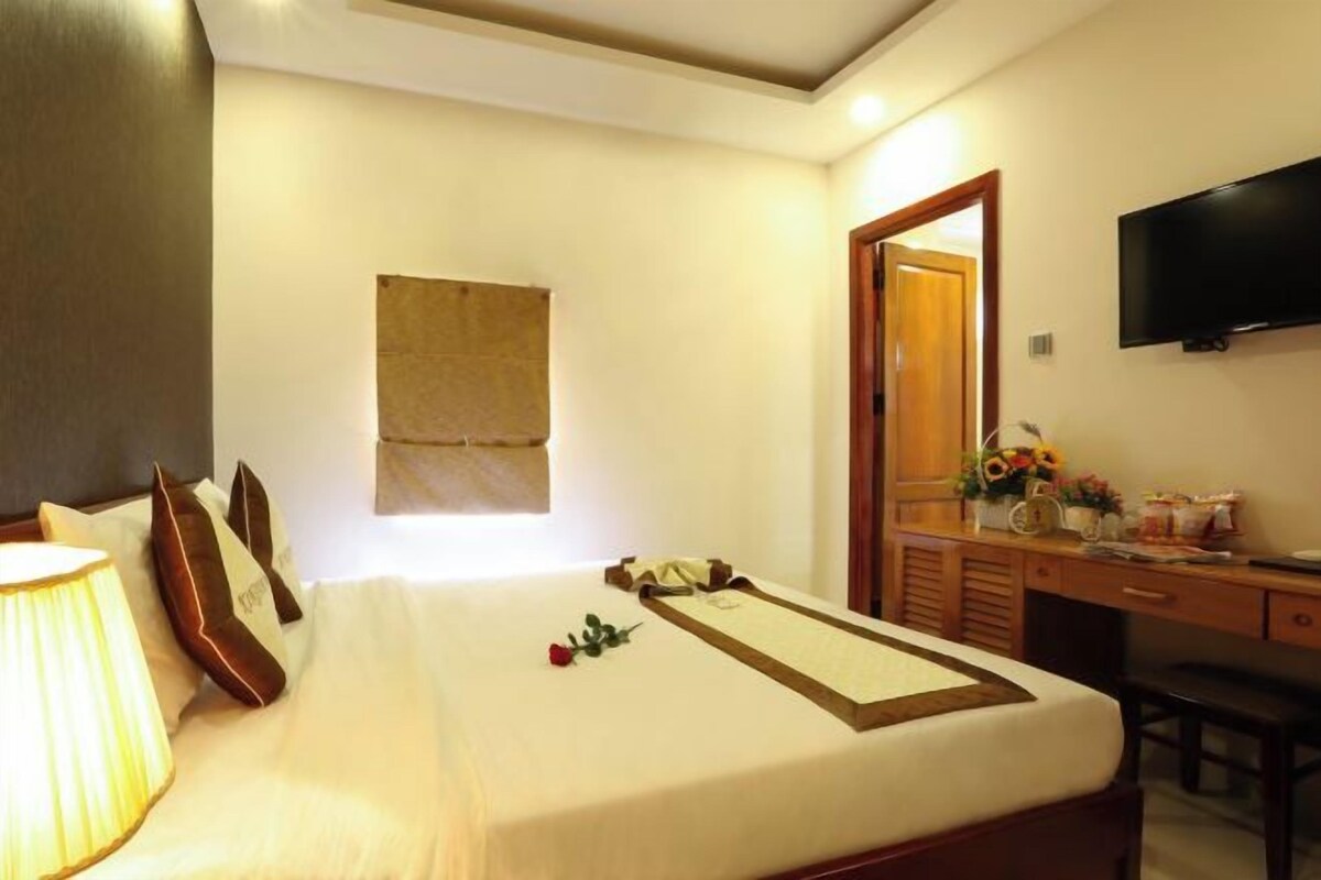 A hotel room with a bed, bedside lamp, a flat-screen TV, a desk with a chair, and a mirror.