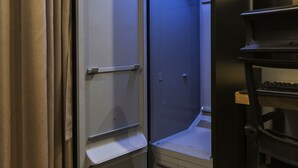 A compact, modern room with a built-in shower, a small desk, and a chair. - Karat Hotel (Busan)
