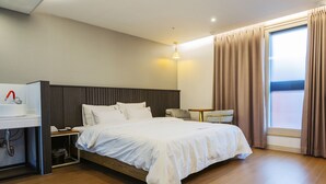 A modern hotel room with a wooden floor, a large bed with white bedding, a desk with a computer, and a window with curtains. - Karat Hotel (Busan)