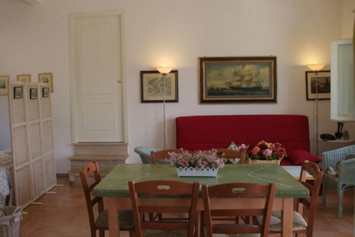 Un coin repas avec une table dressée pour quatre personnes, un canapé rouge et des œuvres d’art encadrées accrochées aux murs.