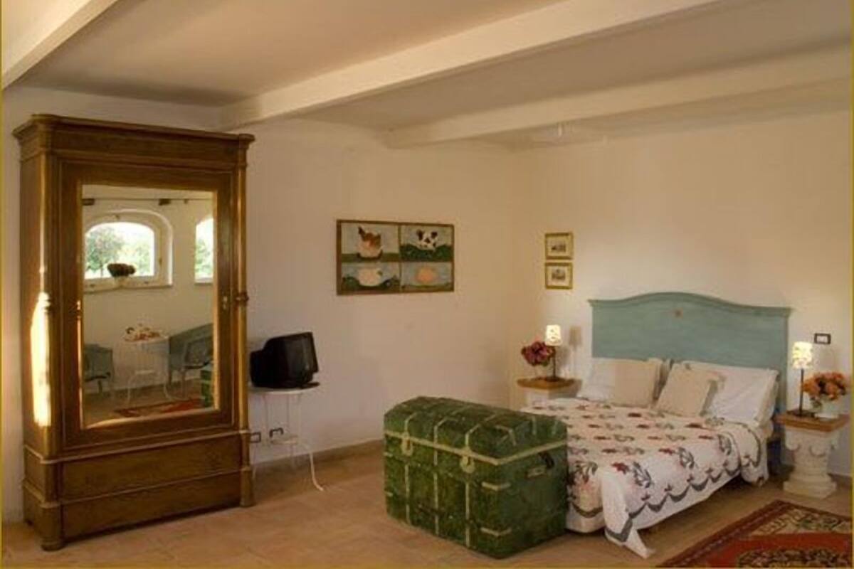 Une chambre à coucher avec un lit, une commode, une malle verte et un tableau accroché au mur.