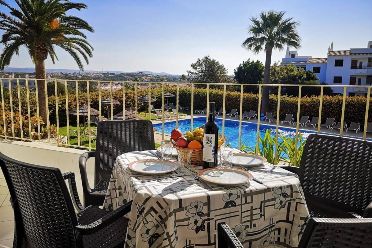 An outdoor dining area with a table set for two, overlooking a swimming pool and a scenic view of hills and buildings.