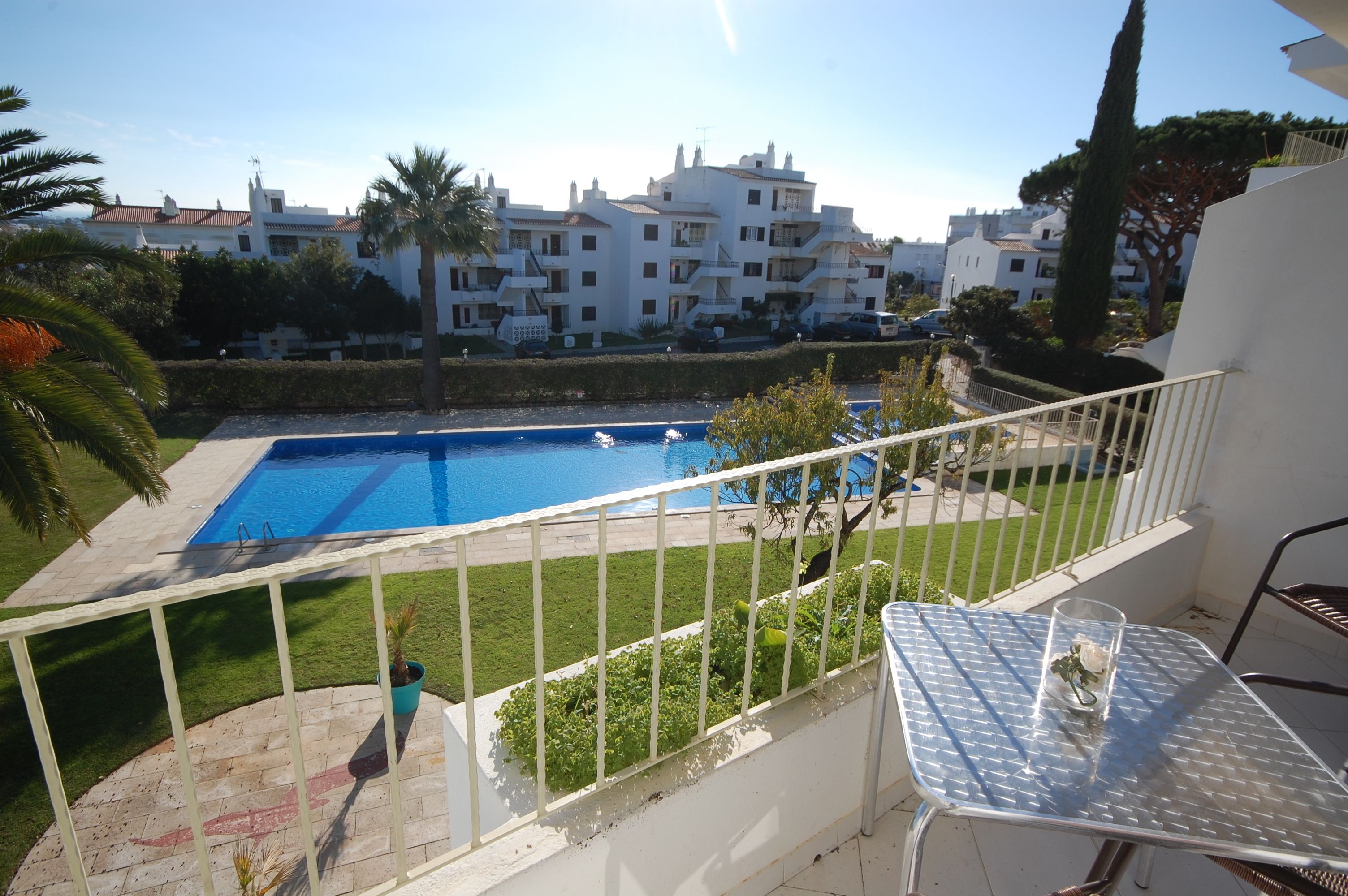 A balcony with a view of a swimming pool, a table with a glass, and a railing.