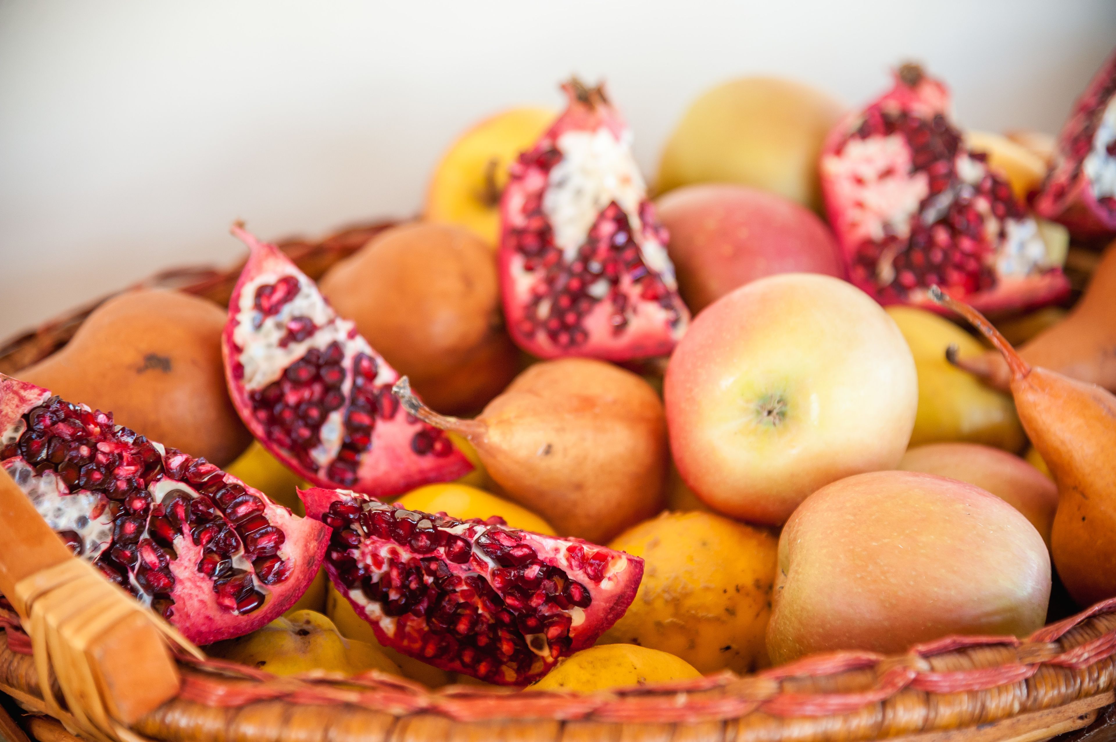 Ein Korb voller verschiedener Früchte, darunter Granatäpfel, Äpfel und Orangen.
