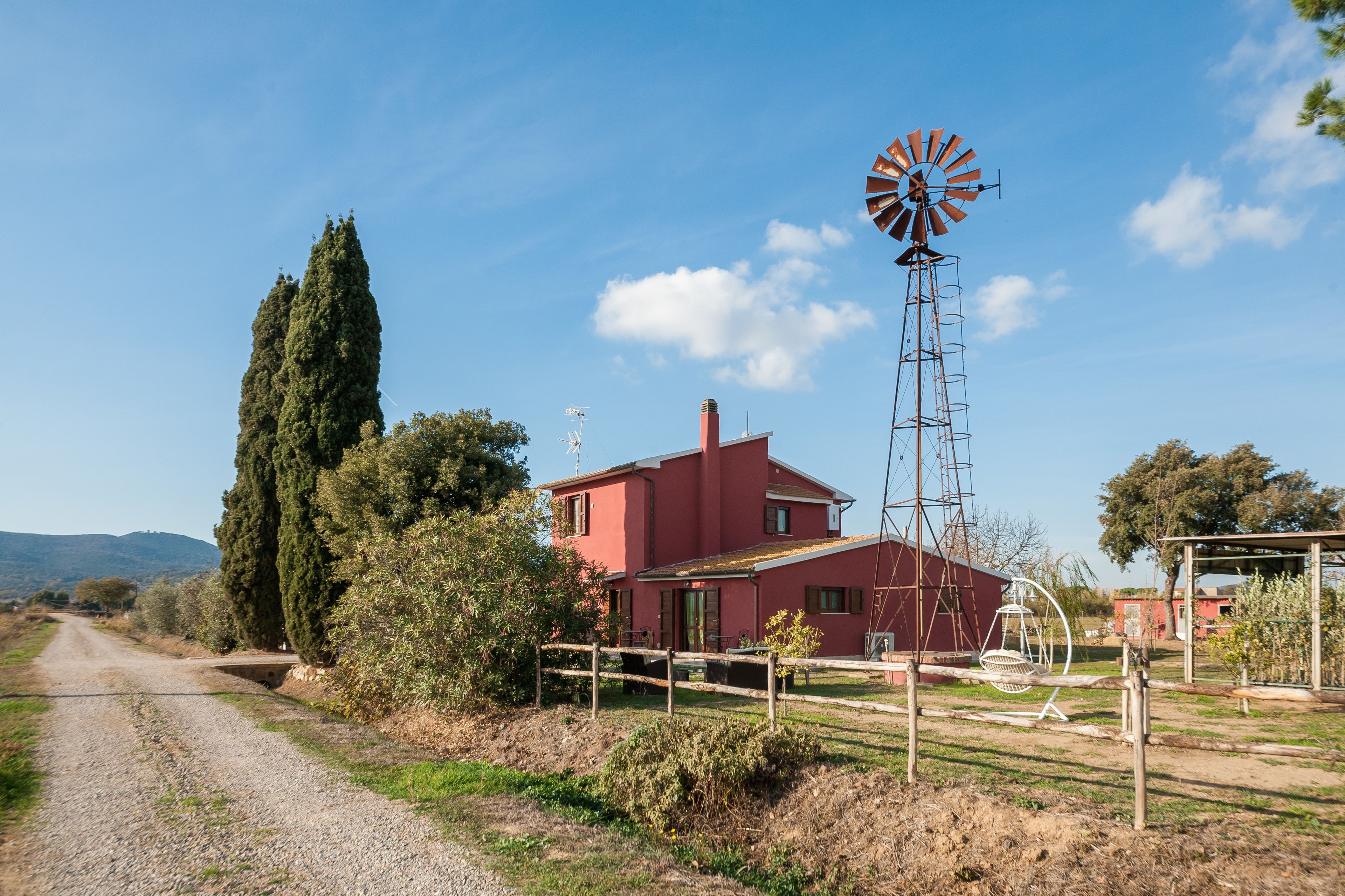 Un camino rural que lleva a una casa roja con un molino.