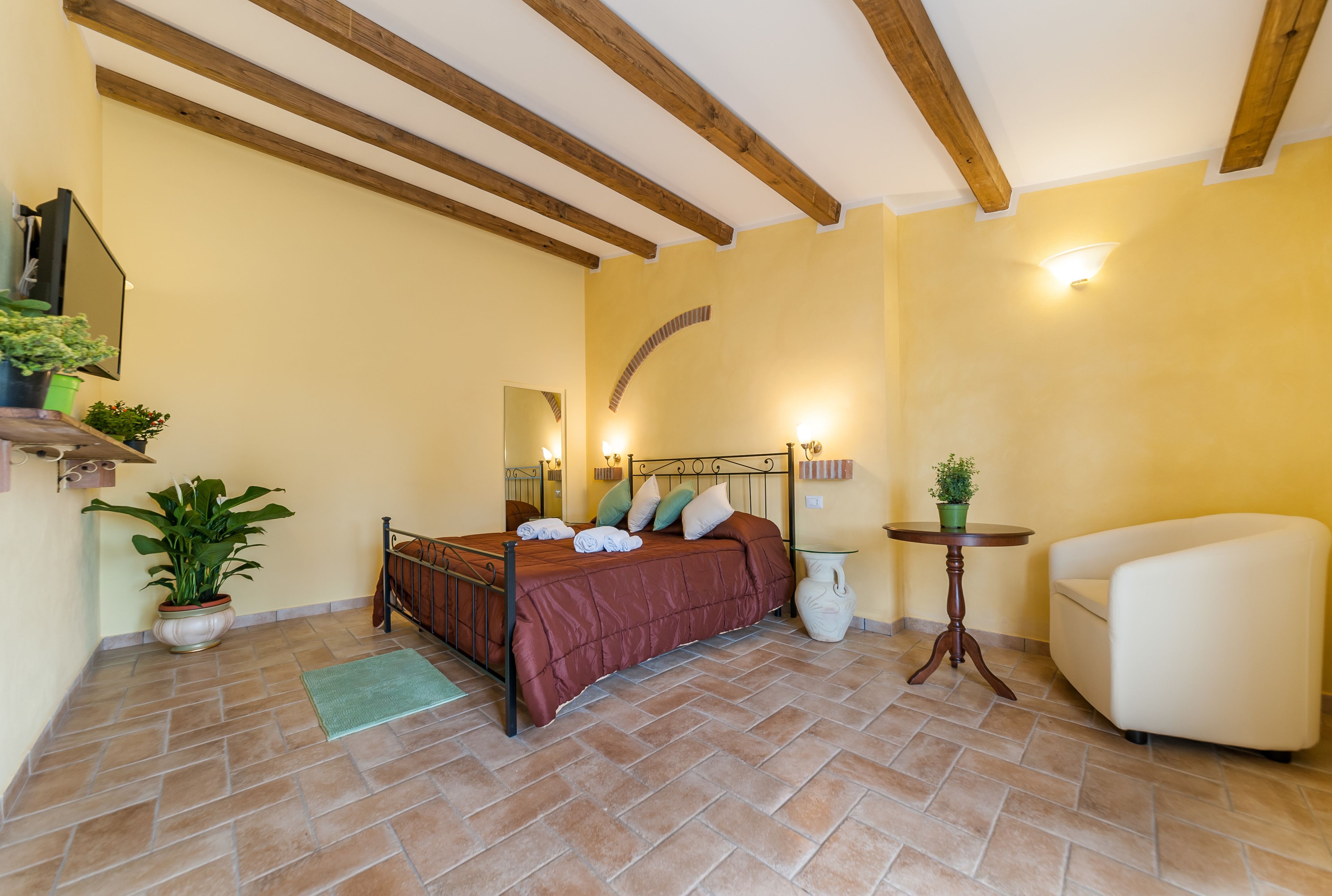 A bedroom with a bed, a chair, a small table, and a potted plant.