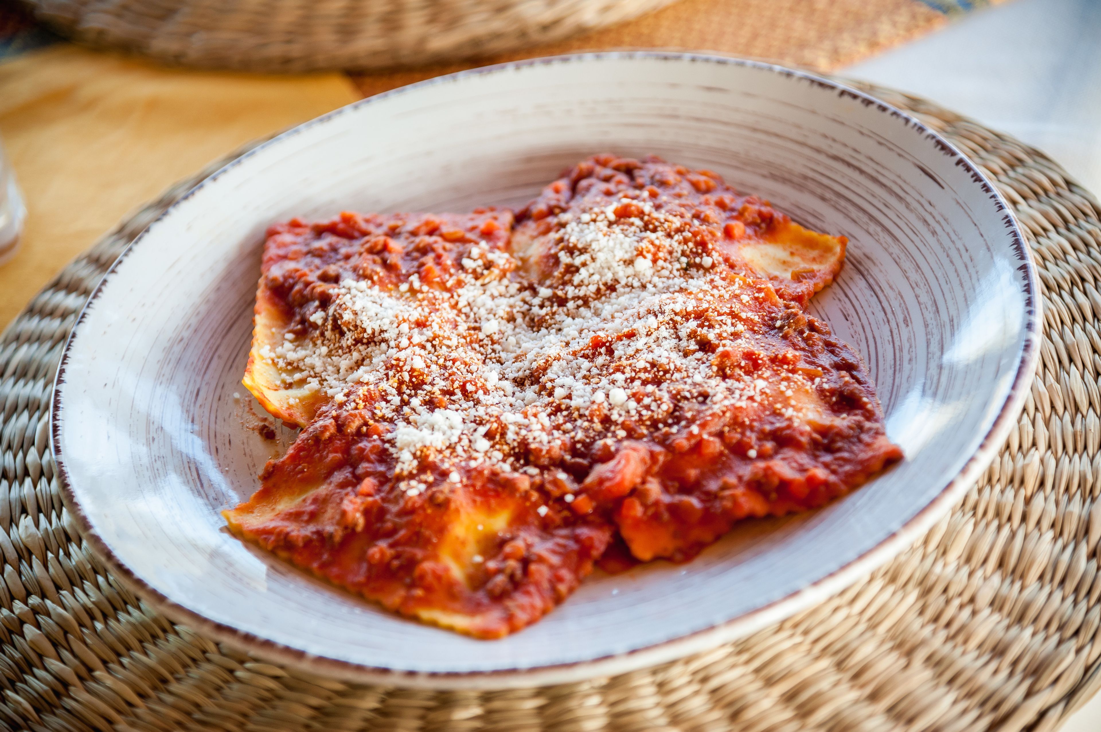 Een bord ravioli met tomatensaus en geraspte kaas op een geweven placemat.