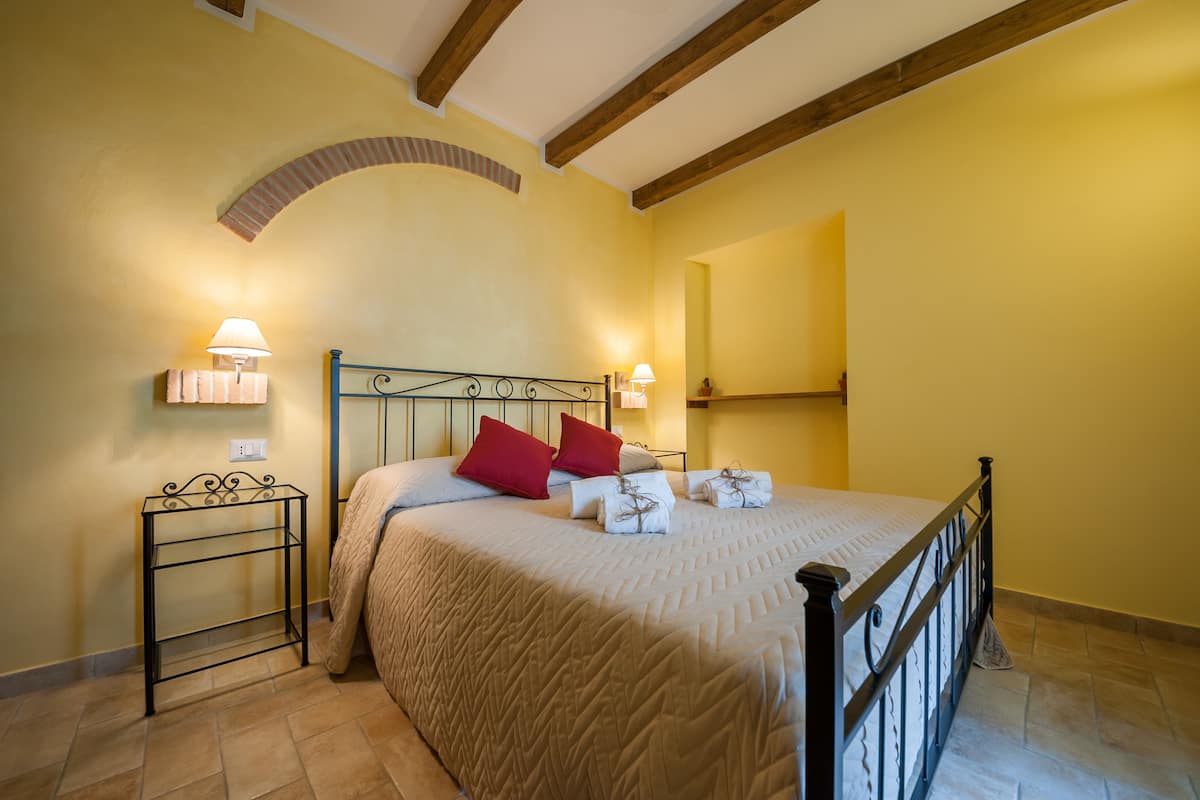 Un dormitorio con una cama, dos mesitas de noche con lámparas, un espejo y suelo de baldosas.