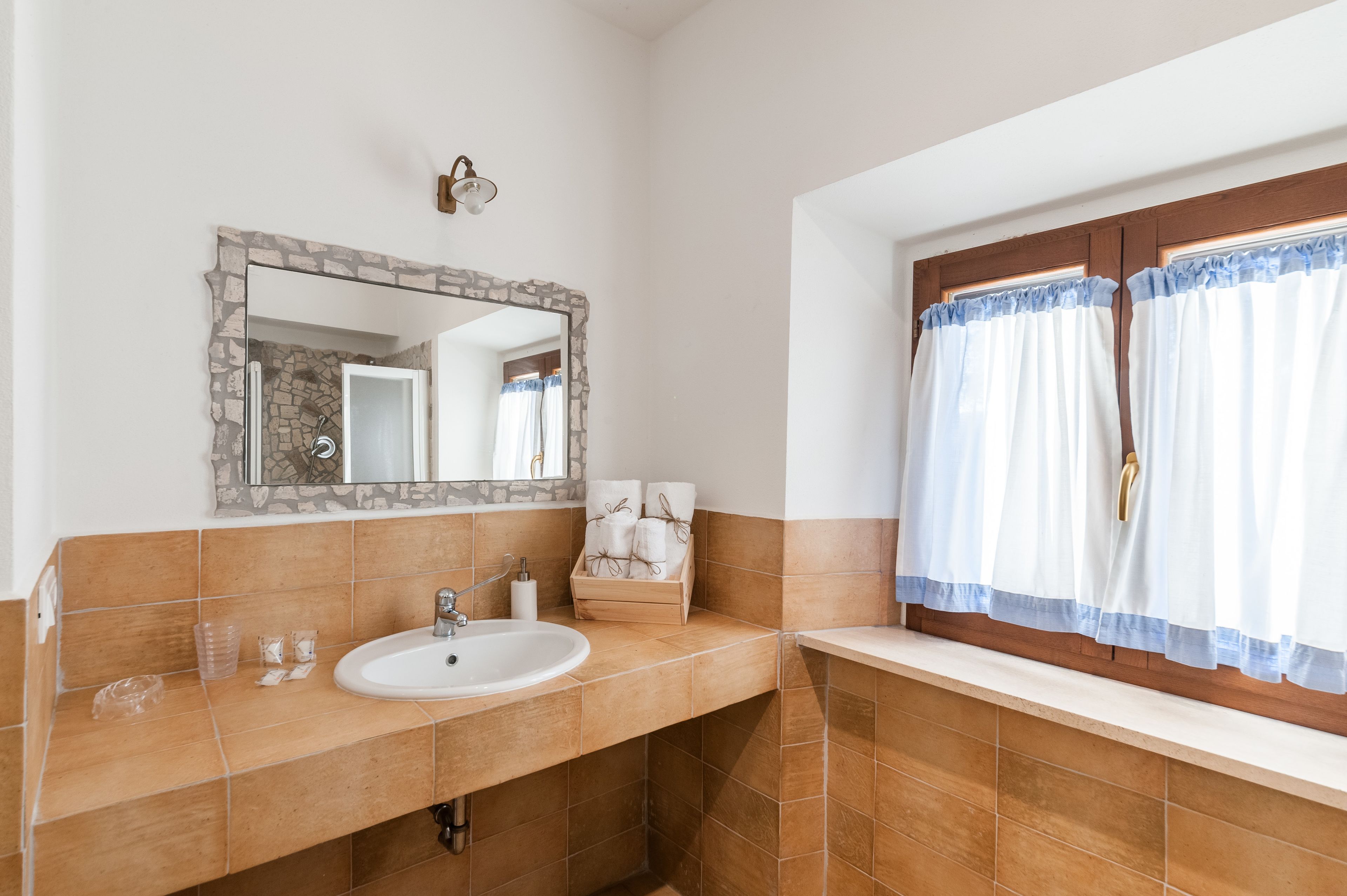 A bathroom with a sink, mirror, and window with curtains.