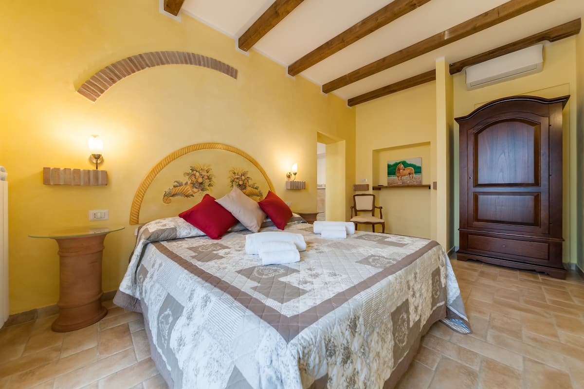 Un dormitorio con una cama grande, dos lámparas de noche, un cabecero de madera, una mesita y una puerta.