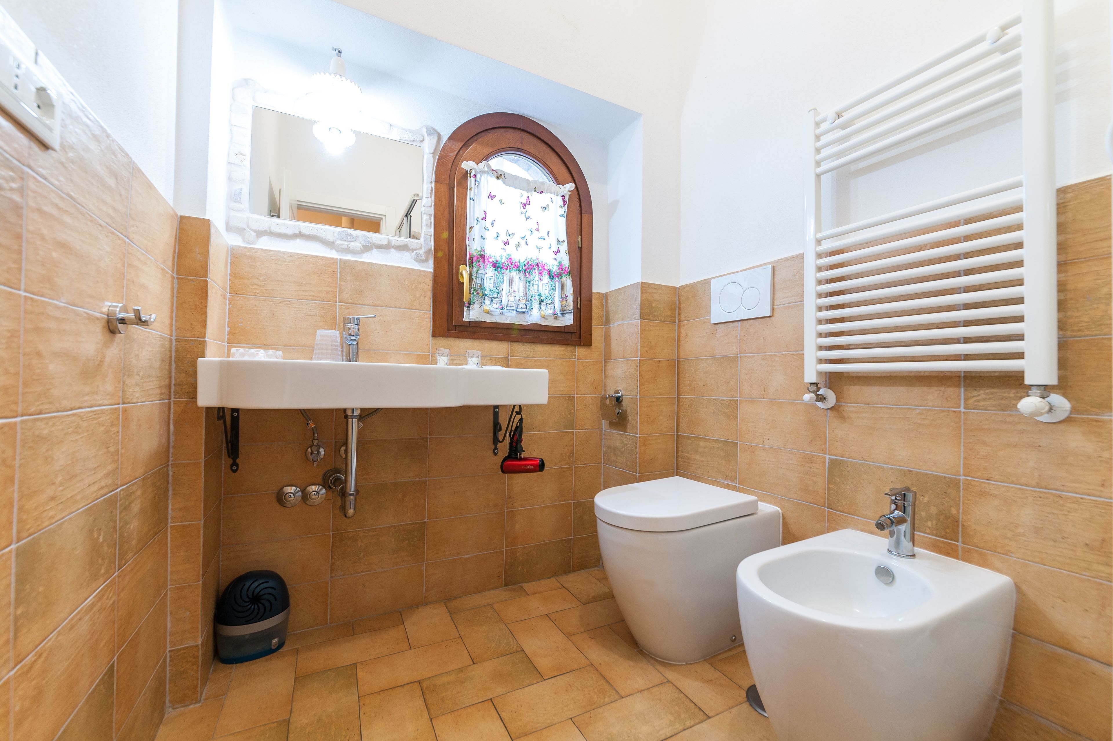 A bathroom with a sink, toilet, bidet, and a window with a curtain.
