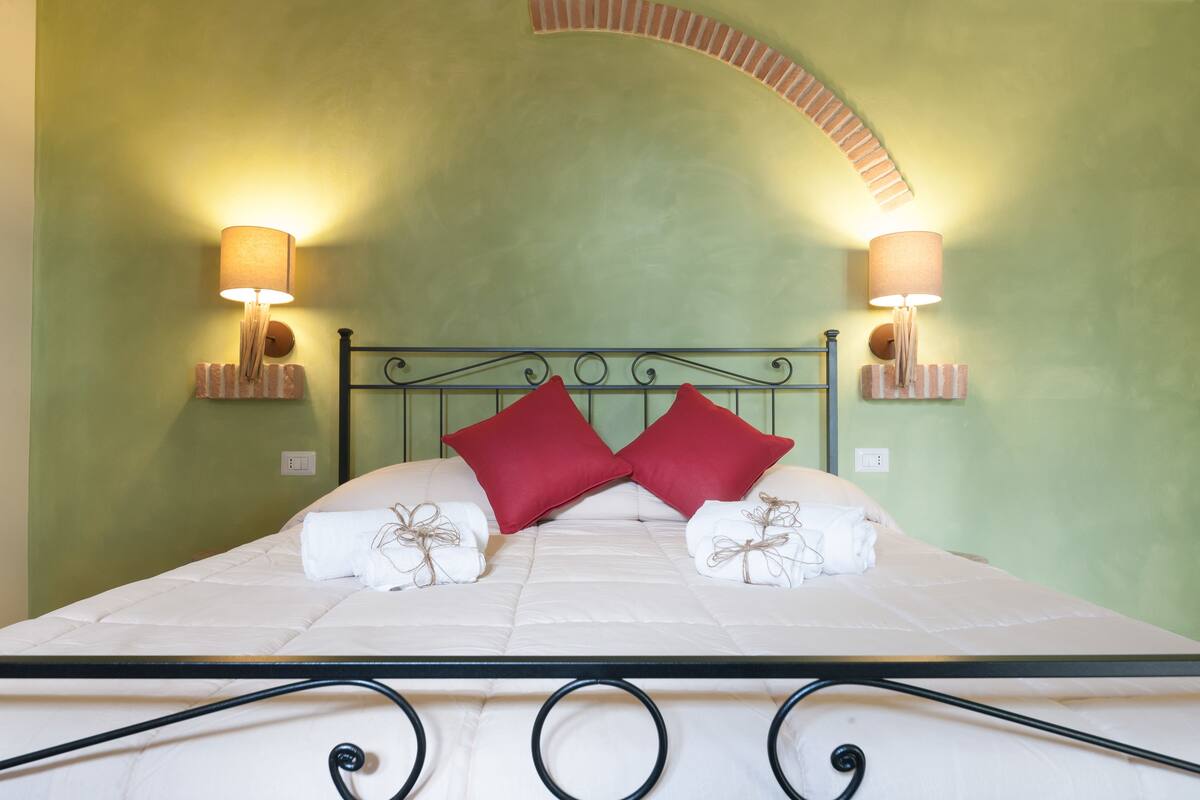 Una cama con estructura metálica, dos almohadas rojas y dos toallas blancas atadas con un hilo.