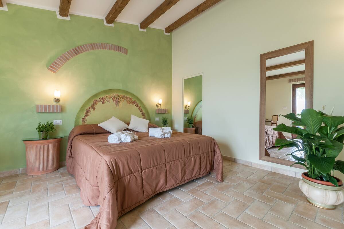 Un dormitorio con una cama grande, paredes verdes y un espejo.
