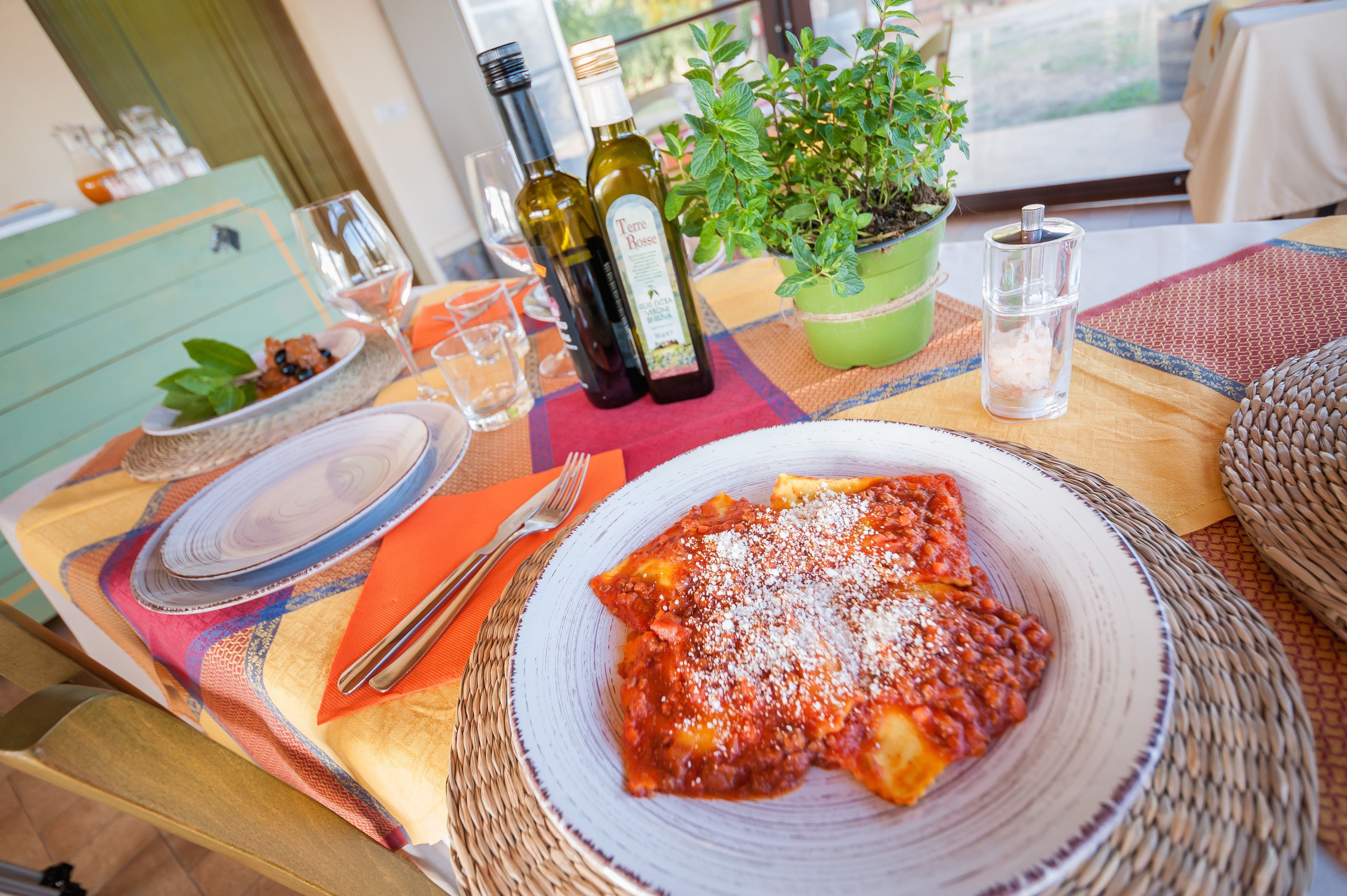 A table with a plate of pasta, wine bottles, glasses, and a potted plant.