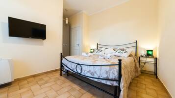 Un dormitorio con cama, televisor de pantalla plana montado en la pared, mesita de noche con lámpara y una puerta que da a otra habitación.