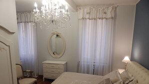 A bedroom with a large bed, a dresser, a chair, a mirror, and a chandelier.