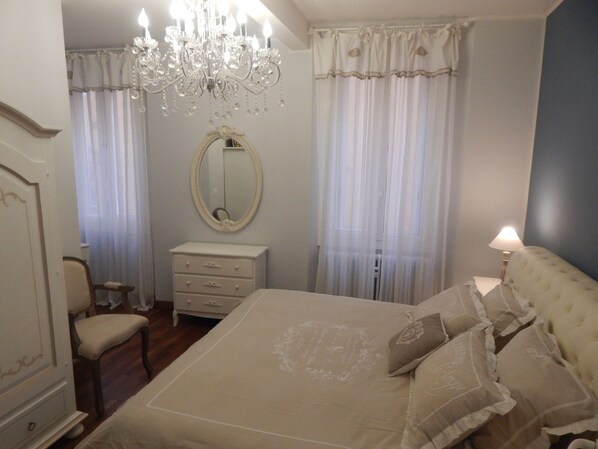 A bedroom with a large bed, a dresser, a chair, a mirror, and a chandelier.