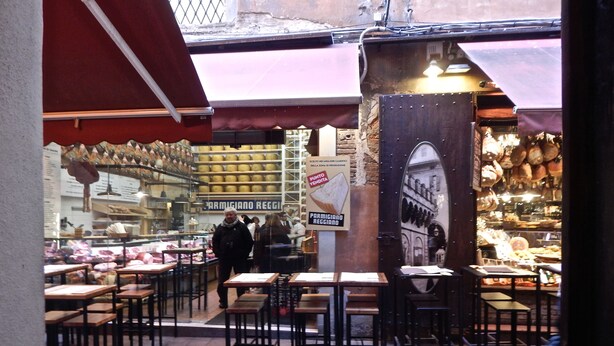 An outdoor café with tables and chairs, a cheese display, and a sign for Parmigiano Reggiano cheese.