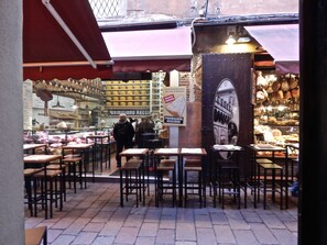 An outdoor café with tables and chairs, a cheese display, and a sign for Parmigiano Reggiano cheese.
