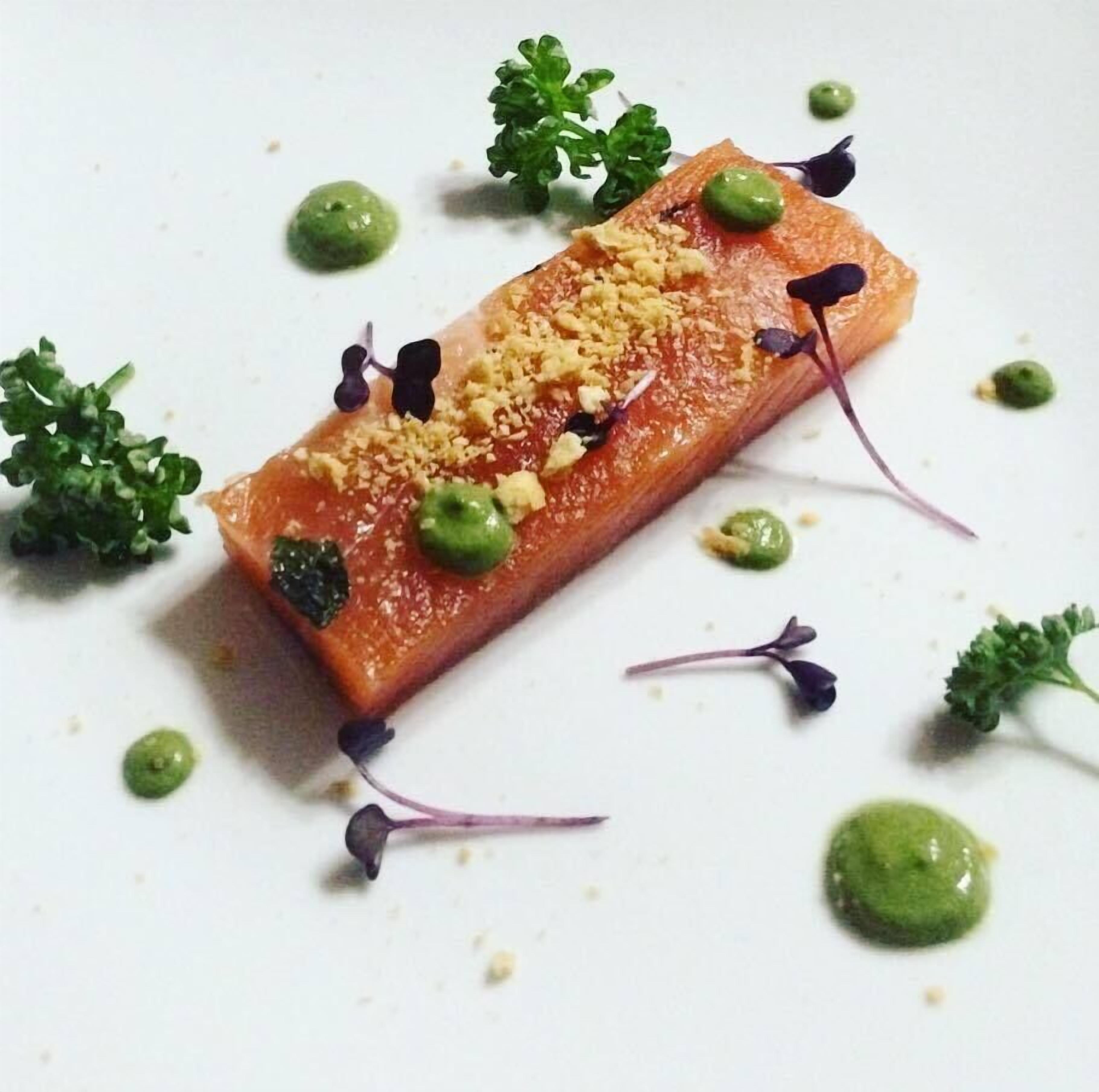 A dish of salmon with green sauce and garnishes on a white plate.