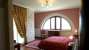 A bedroom with a large bed, a desk, a chair, a window with a curved arch, and a chandelier. - Villa Flora Baia degli Ulivi (Santeramo in Colle)