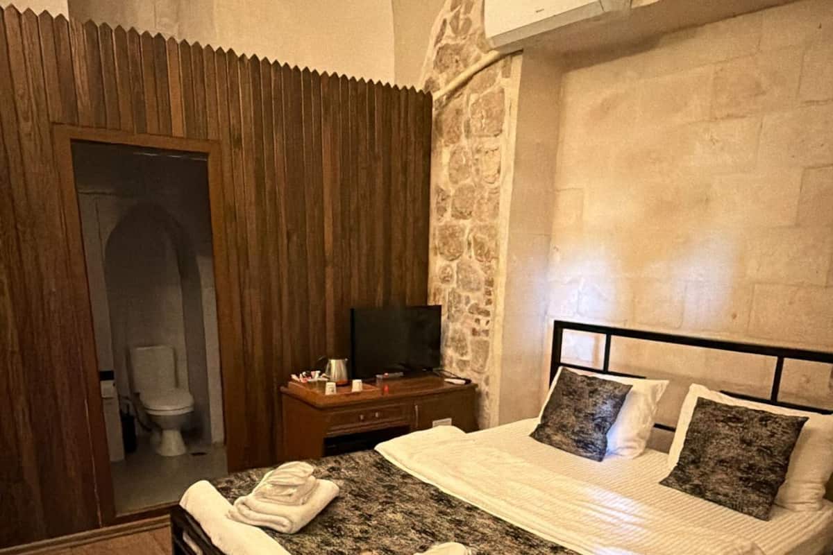 A bedroom with a bed, a television, a stone wall, and a wooden floor.