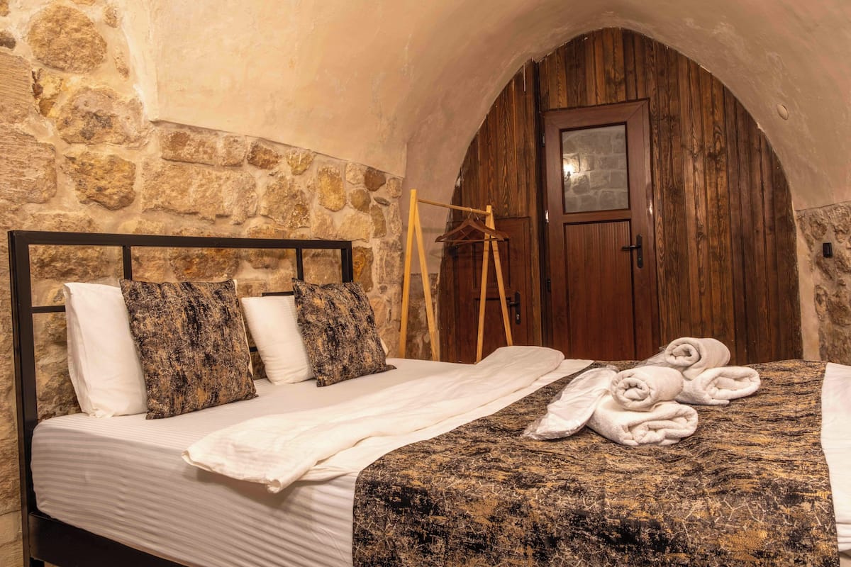 A bedroom with a stone wall, wooden door, and a bed with white and patterned bedding.